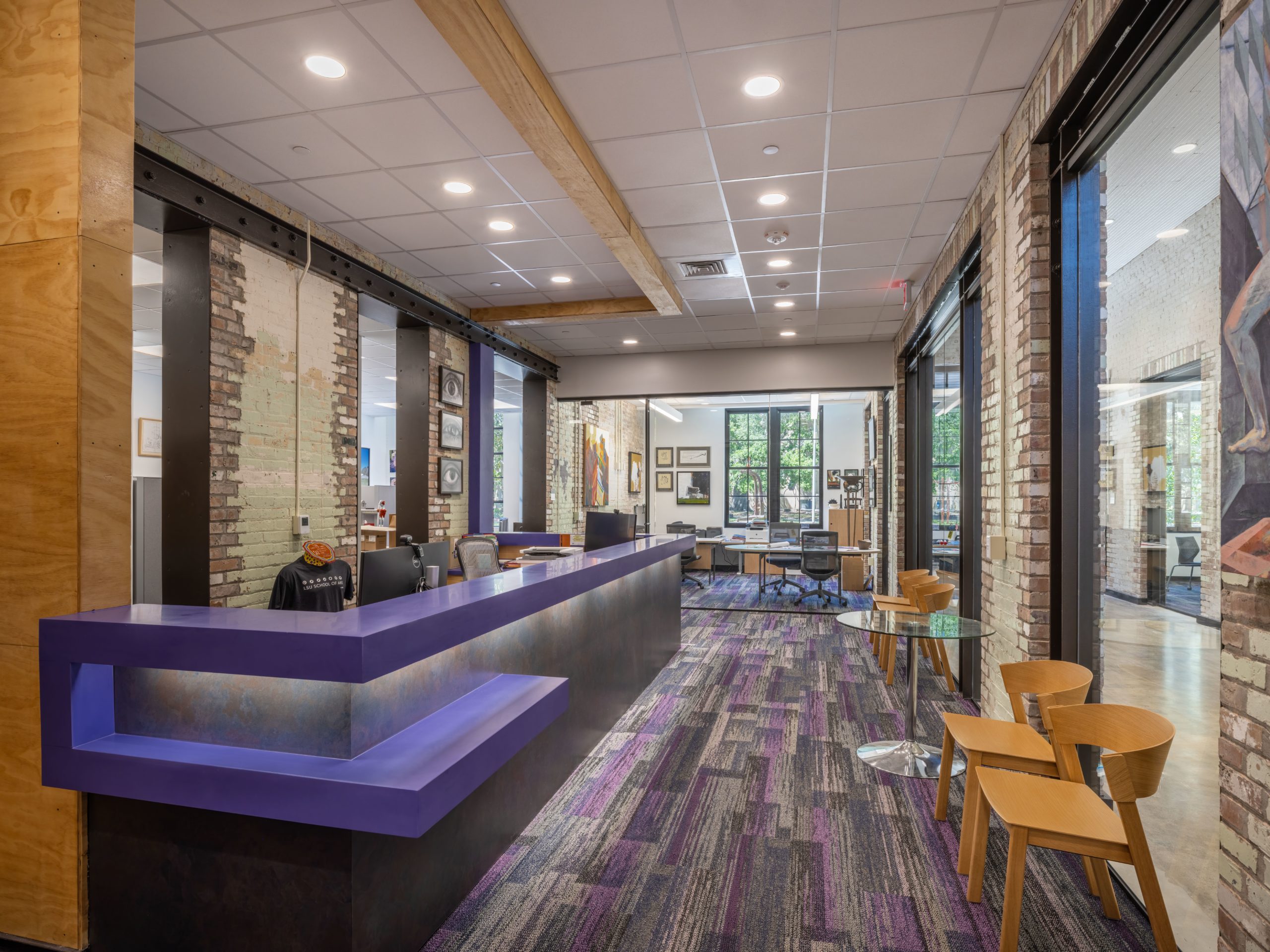 Modern office reception area design with a vibrant purple desk, exposed brick, and contemporary interior finishes. Commercial architectural space for welcoming visitors, featuring an open layout and a dynamic patterned carpet.
