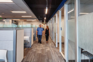 man-woman-walking-hallway-with-cubicles-glass-doors
